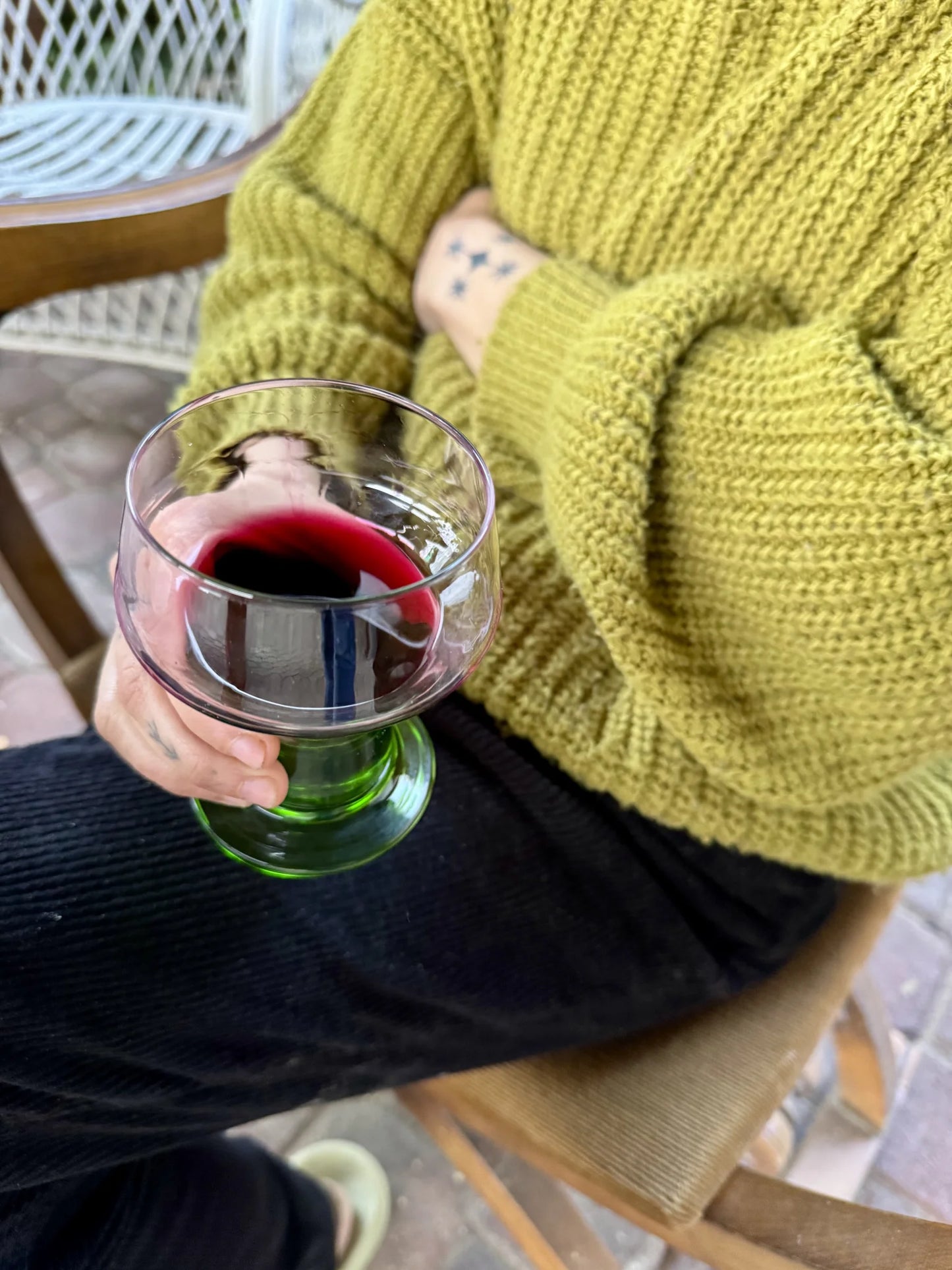 Bicchiere in vetro con base verde – tenuto in mano con dentro del vino rosso