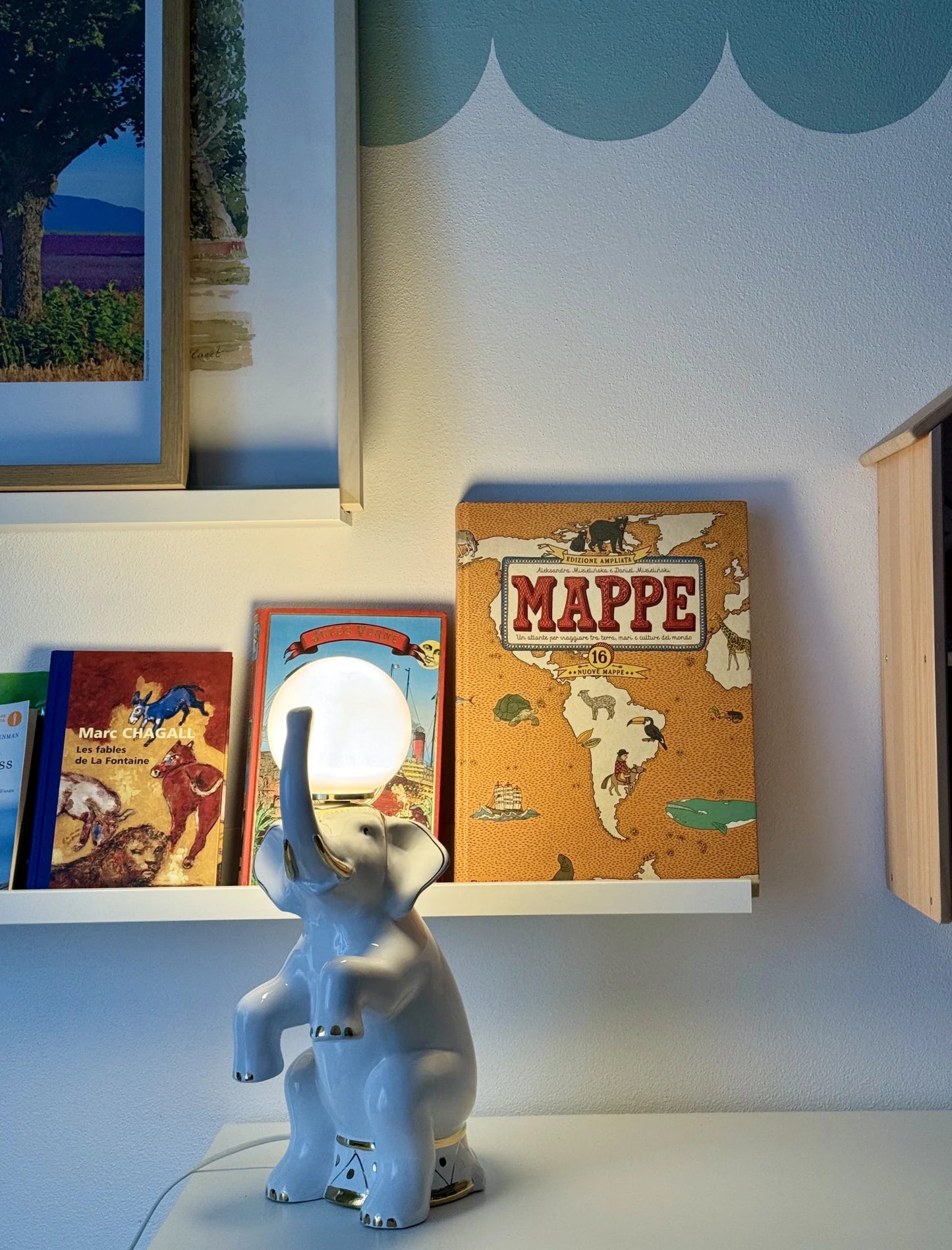 Lampada in ceramica bianca a forma di elefante – accesa sopra uno scaffale bianco con libri