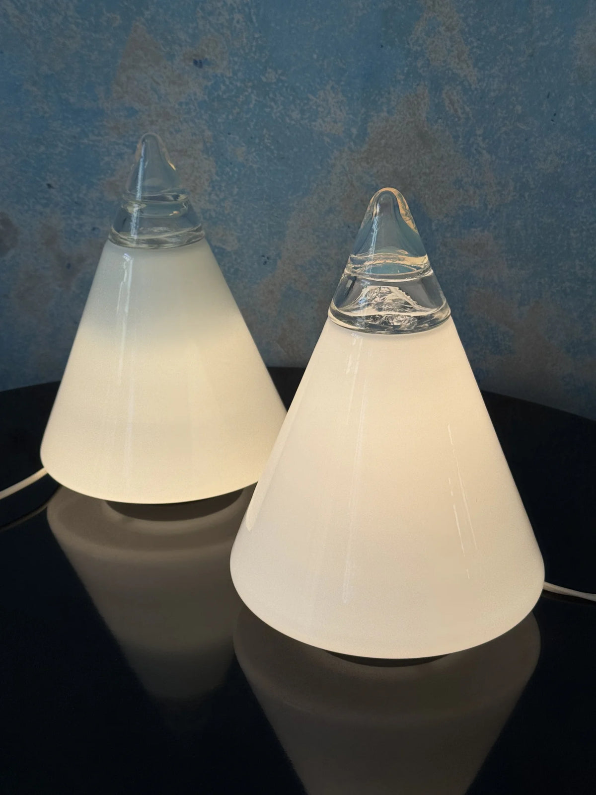 Coppia lampade coniche in vetro bianco Leucos – entrambe accese appoggiate su piano nero