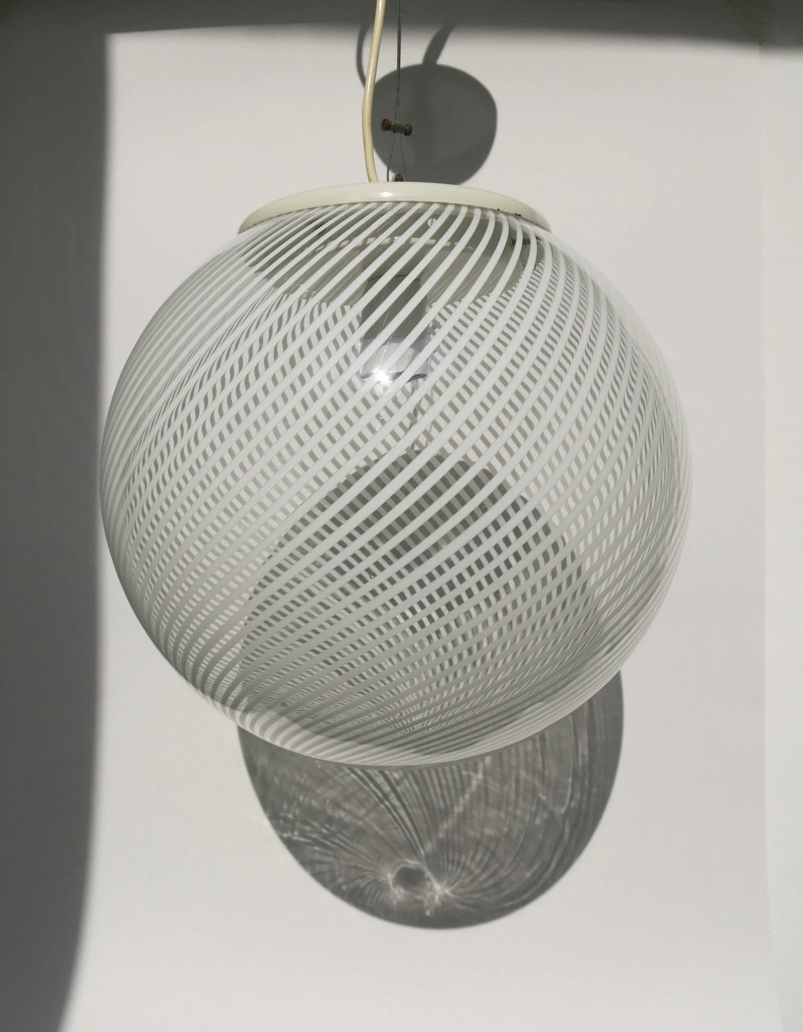 Lampadario a sfera in vetro soffiato – motivo a canne bianche con ombra proiettata sulla parete