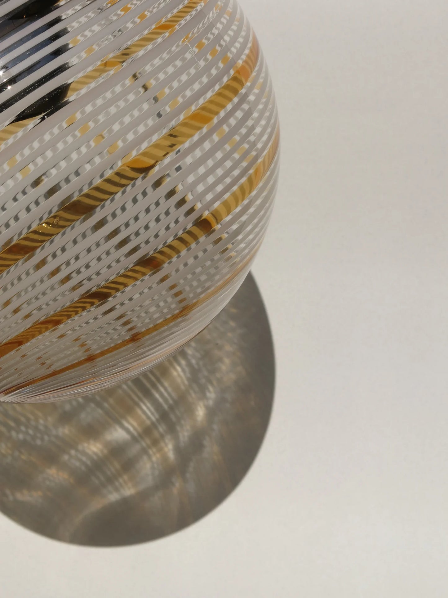 Lampadario di Murano a sfera in vetro soffiato – vista laterale con filigrana a spirale bianca e oro, luce naturale