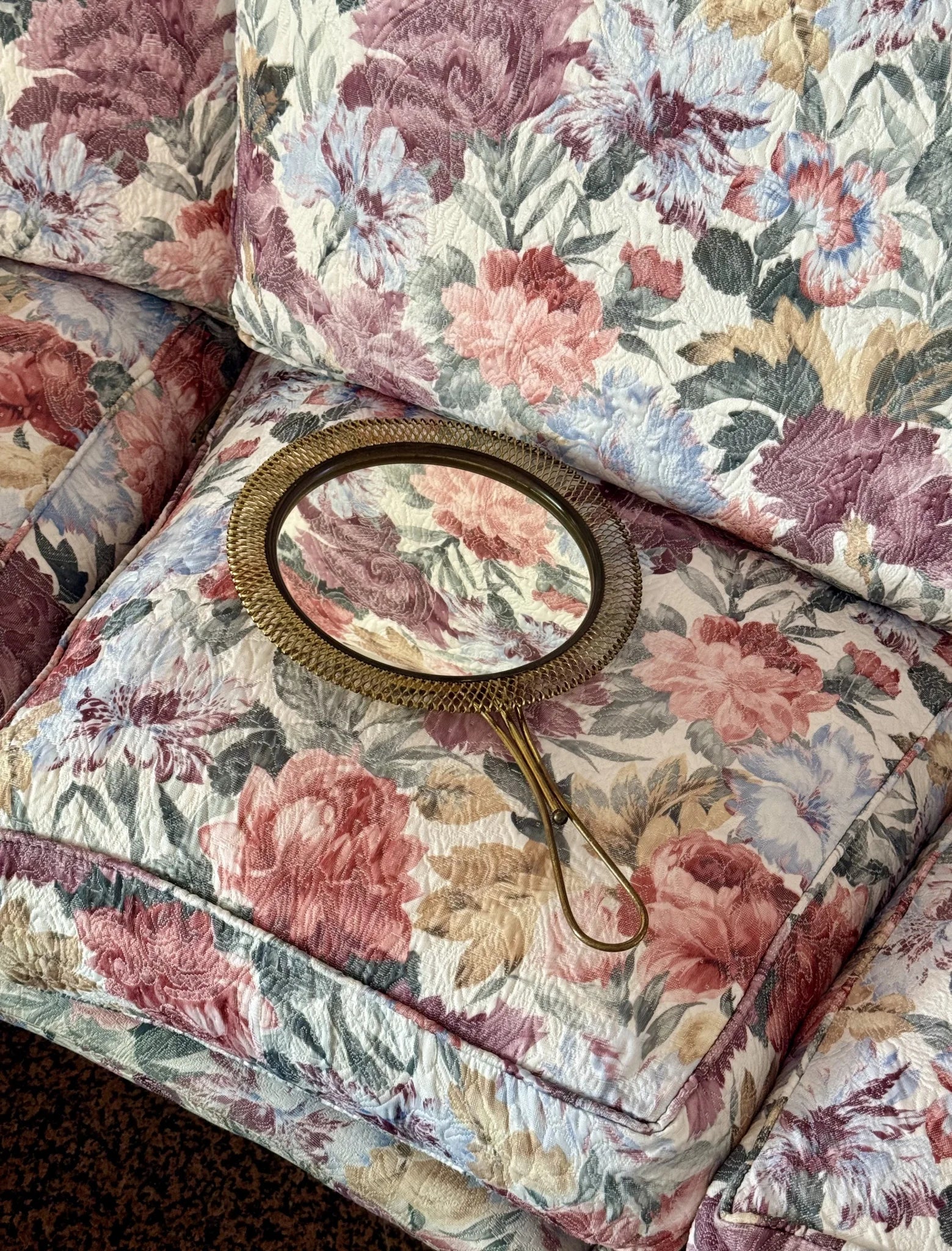 Specchio a mano in ottone traforato – appoggiato su divano a fiori