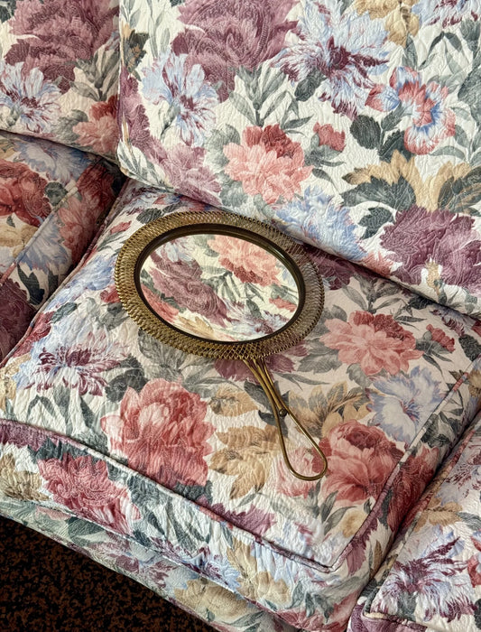 Specchio a mano in ottone traforato – appoggiato su divano a fiori