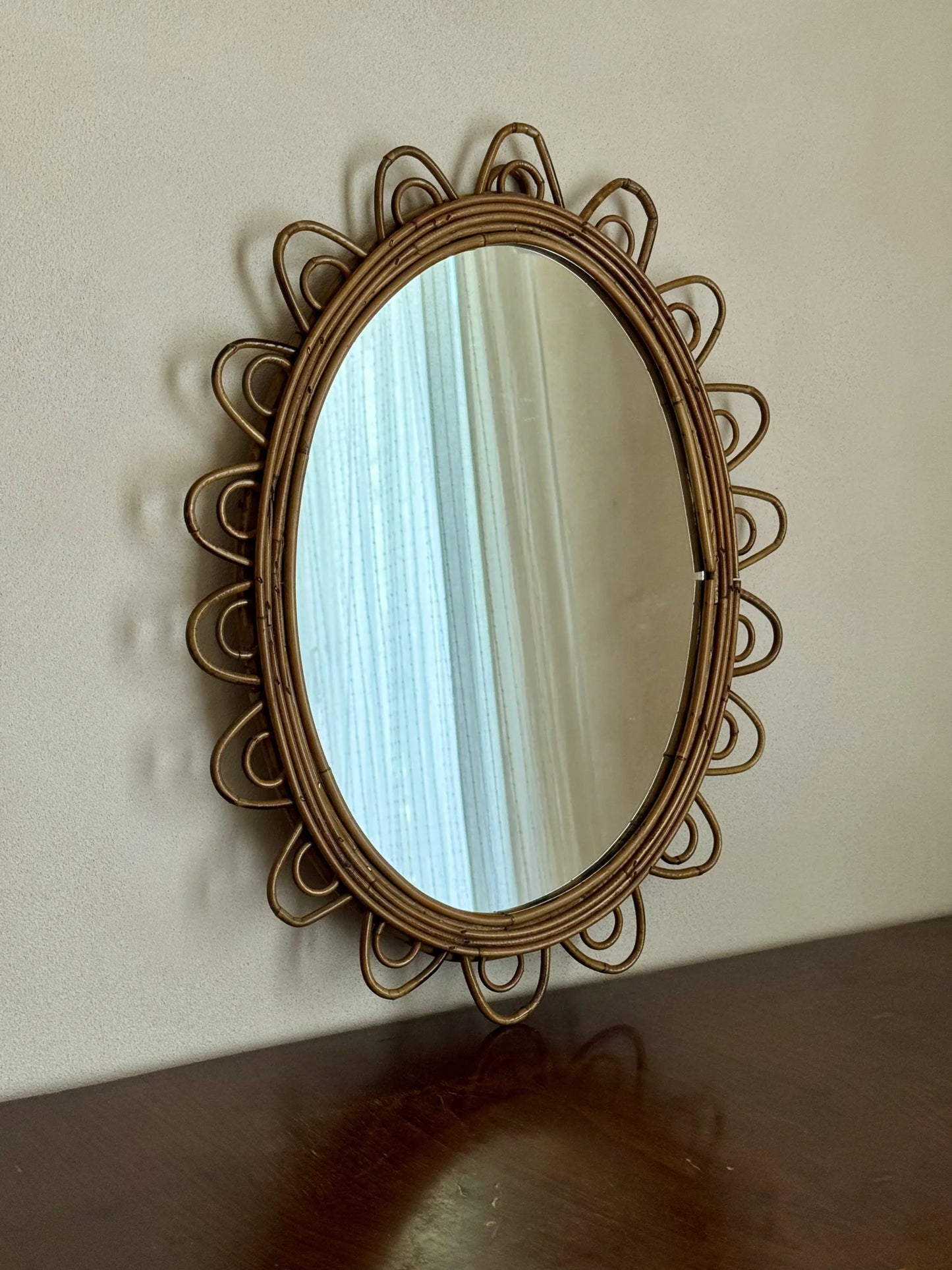 Specchio ovale in rattan con cornice smerlata – appoggiato sopra un mobile con riflessa una tenda leggera