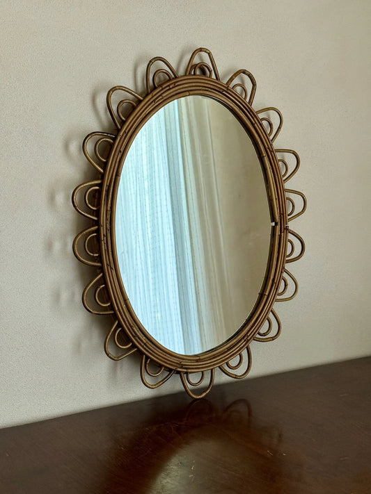 Specchio ovale in rattan con cornice smerlata – appoggiato sopra un mobile con riflessa una tenda leggera