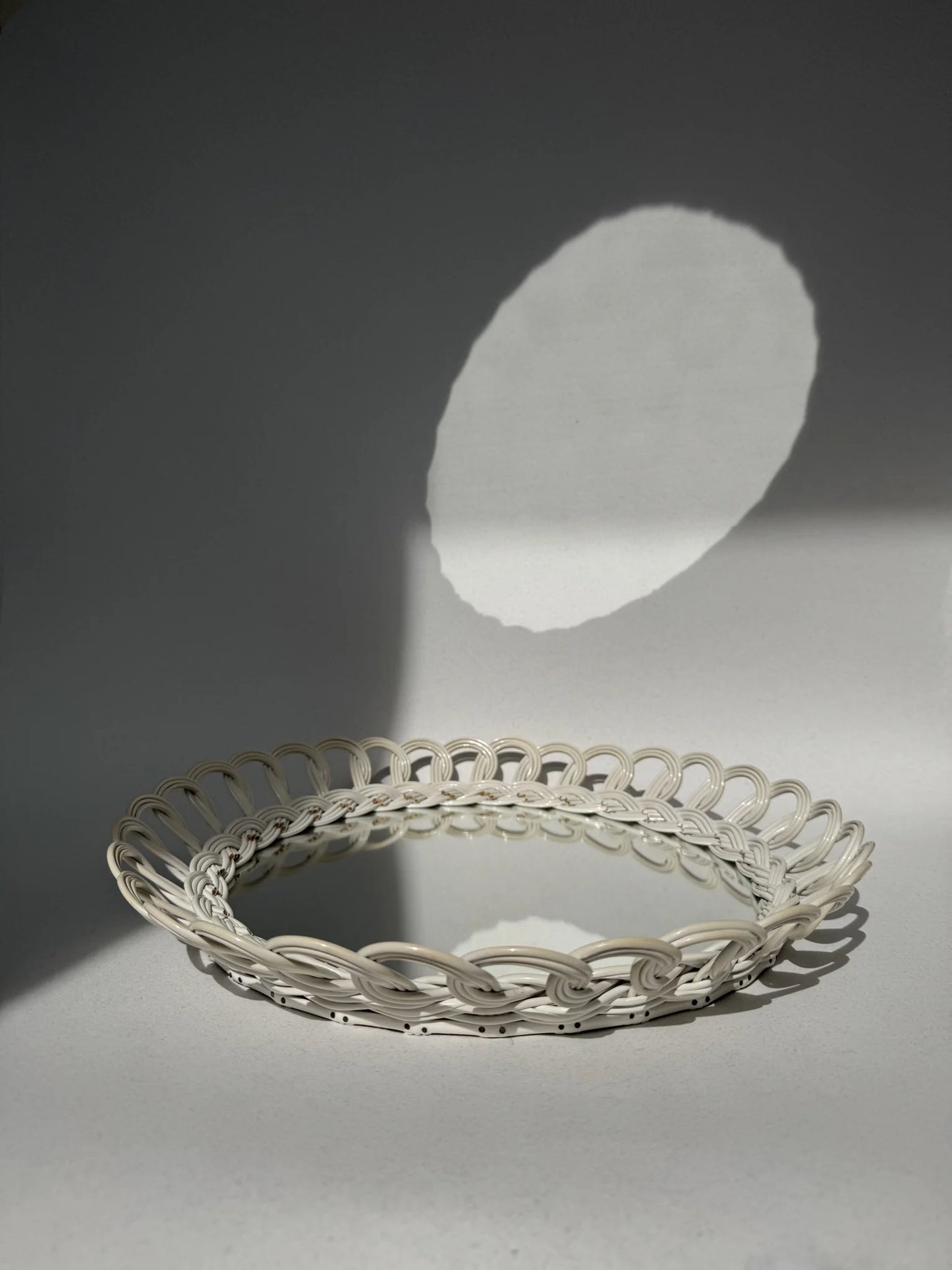 Specchio rotondo con cornice in plastica intrecciata bianca – posato sul piano con ombra proiettata, vista dall'alto