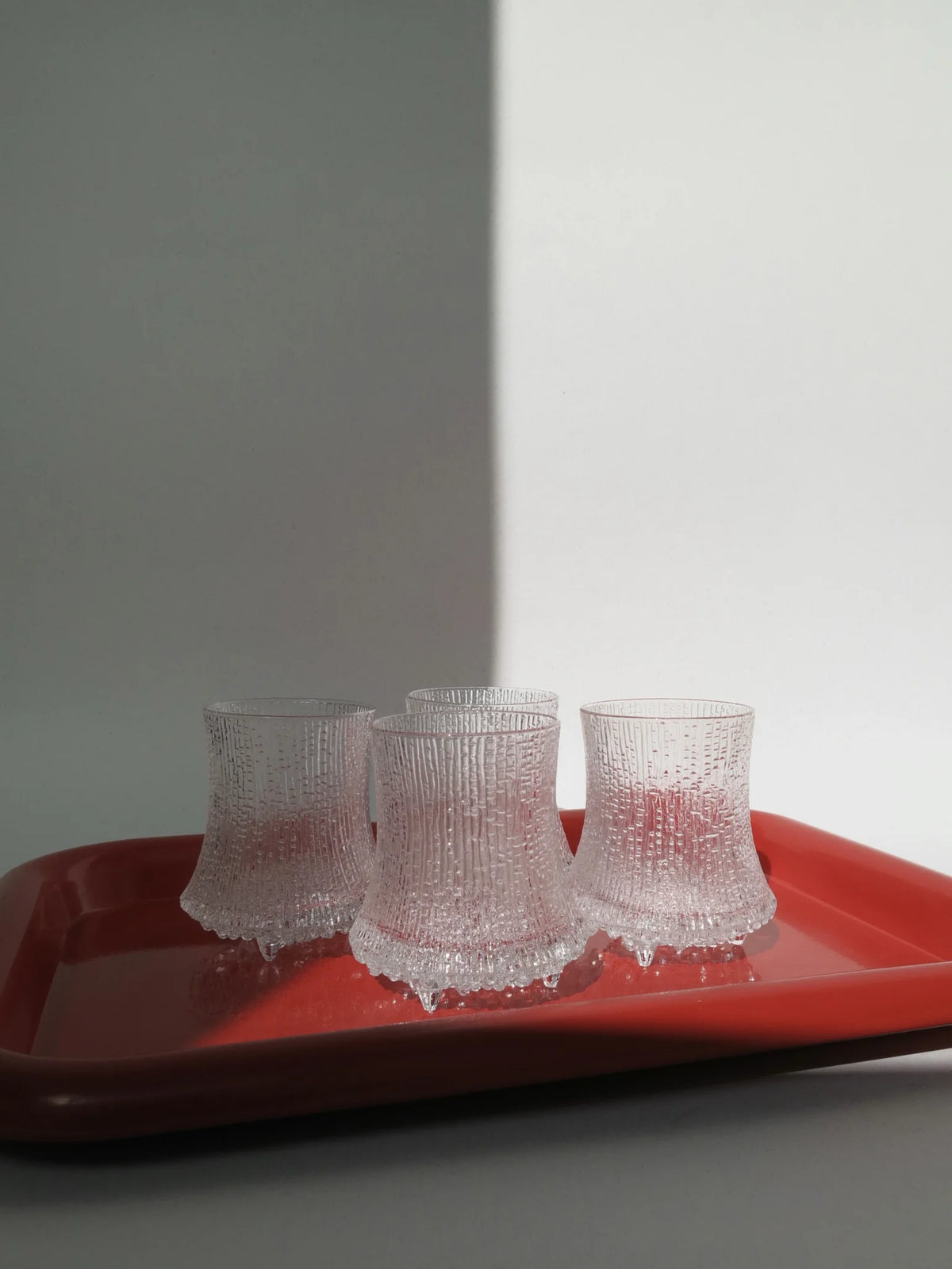 Set di 4 bicchieri acqua modello Ultima Thule di Iittala – ambientati su un vassoio in metallo rosso