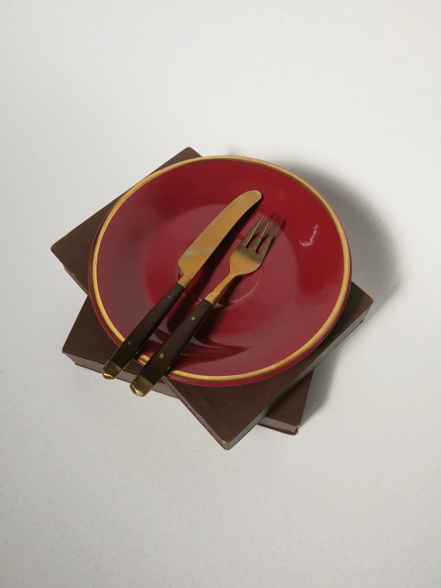 Set posate da frutta in ottone e legno – forchetta e coltello appoggiati su piatto rosso, vista dall'alto