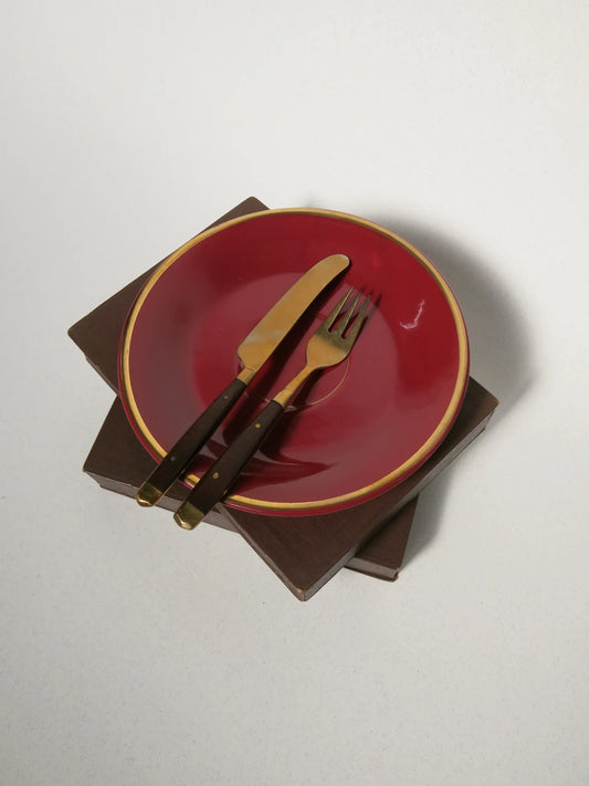 Set posate da frutta in ottone e legno – forchetta e coltello appoggiati su piatto rosso, vista dall'alto
