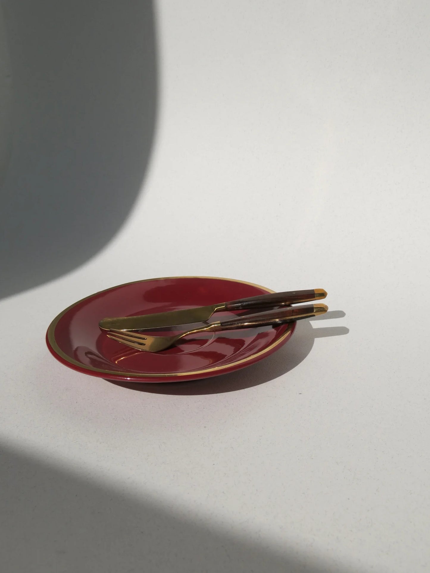 Set posate da frutta in ottone e legno – forchetta e coltello appoggiati su piatto rosso, vista frontale