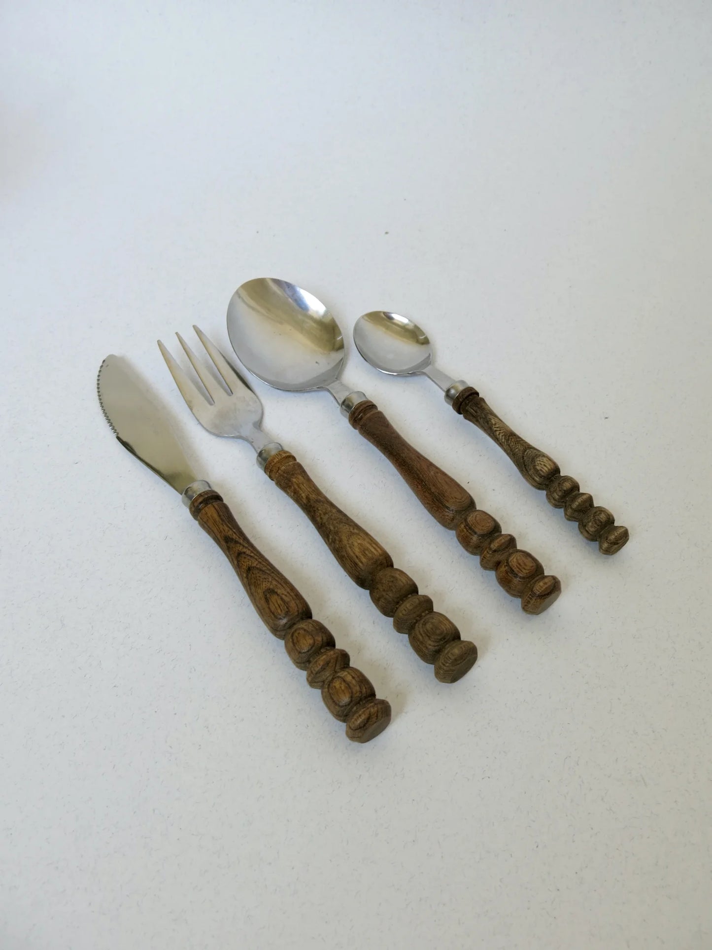 Servizio di posate con manico di legno tornito – coltello, forchetta, cucchiaio e cucchiaino disposti uno di fianco all'altro